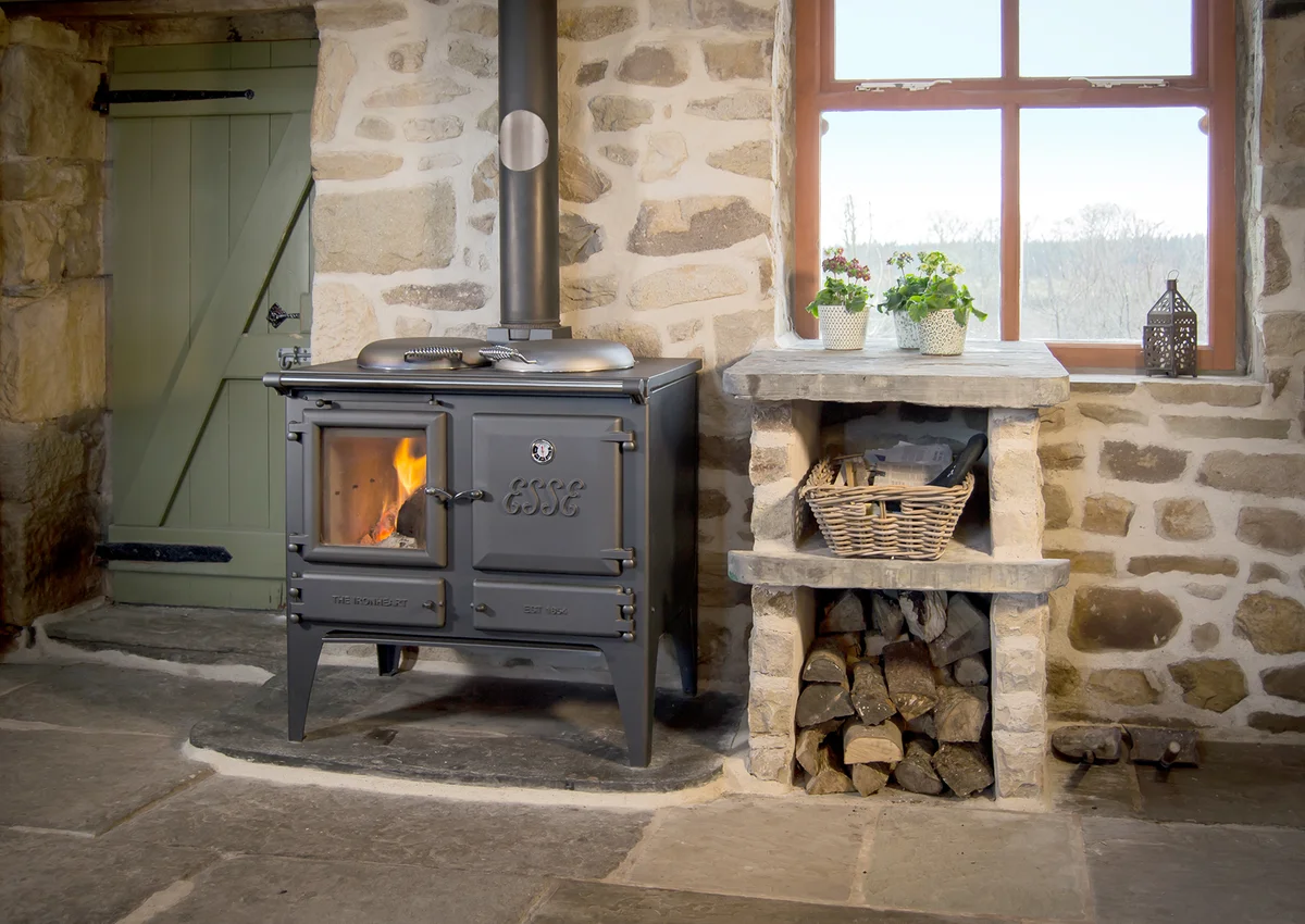 Ein dunkler Ofen der Marke Esse neben einer Sammlung an Feuerholz